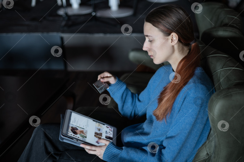 Скачать Девушка сидит в вестибюле отеля или ресторана и делает онлайн-заказ с оплатой кредитной картой через планшет. Современные технологии. фотосток Ozero