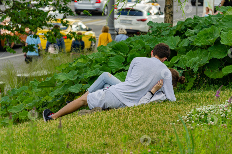 Скачать Парк Зарядье. Парень и девушка лежат на траве и обнимаются на размытом зеленом фоне. Выборочный фокус. Место отдыха москвичей и гостей столицы. Крупный план. фотосток Ozero