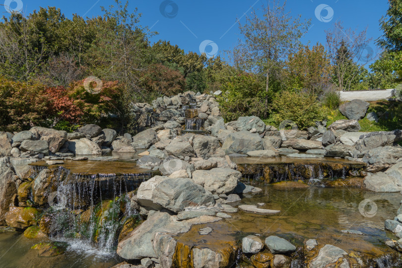 Скачать Тройной водопад в японском саду. Вода падает с высоты 7 метров в искусственное каменистое русло реки. Крупный план. Русло реки делится на три потока, которые превращаются в водопады. фотосток Ozero