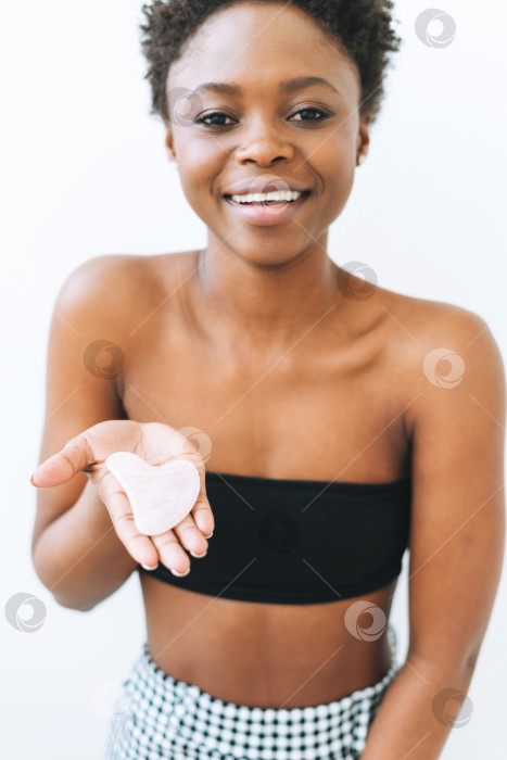 Скачать Красивый портрет красивой молодой афроамериканки с камнем из розового кварца в руках возле лица, изолированного на белом фоне фотосток Ozero