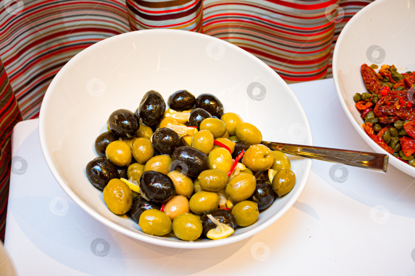 Скачать Смешанные маринованные оливки в белой сервировочной миске фотосток Ozero