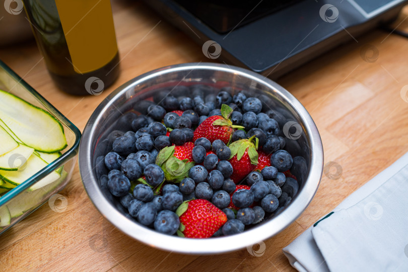 Скачать Глубокая металлическая ваза с ягодами на кухонном столе. Свежая черника и клубника. фотосток Ozero