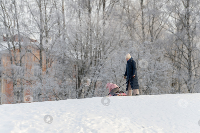 Скачать Мать и ребенок катаются с горки в зимнем парке. Россия, Гатчина, январь 2024 года. фотосток Ozero