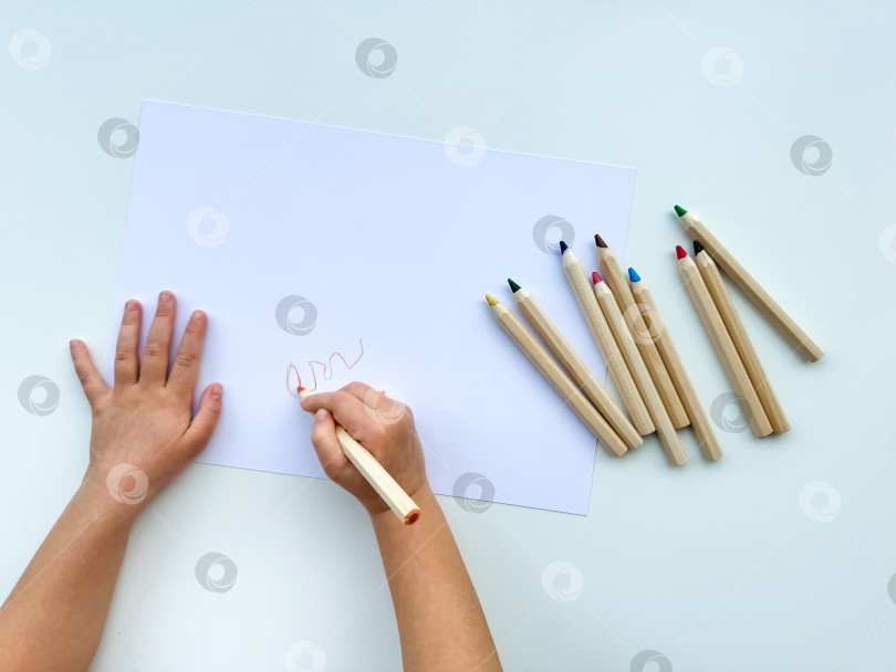 Скачать маленький ребенок рисует цветными карандашами на бумаге на белом столе. фотосток Ozero