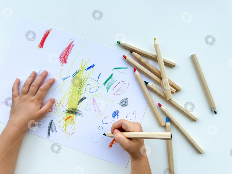 Скачать маленький ребенок рисует цветными карандашами на бумаге на белом столе. фотосток Ozero