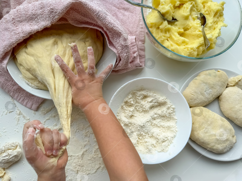 Скачать Руки ребенка месят тесто для выпечки пирогов на белом столе, вид сверху. фотосток Ozero