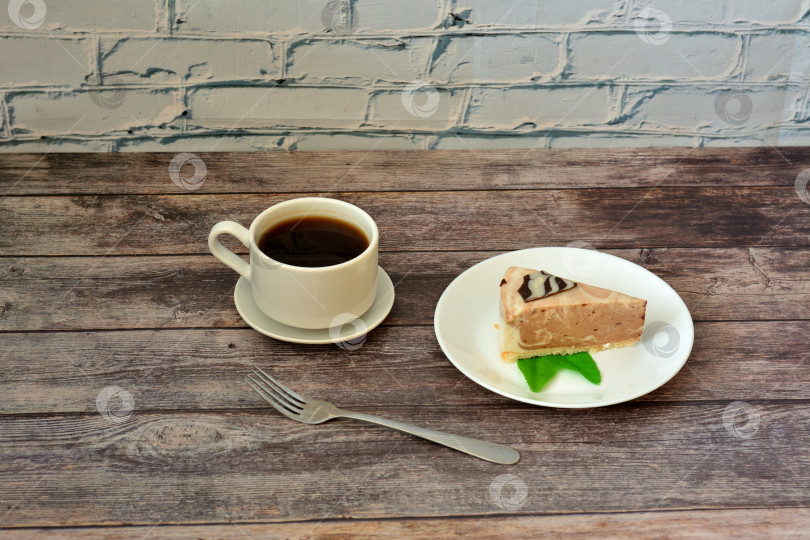 Скачать Тарелка с ломтиком свежего сливочного чизкейка с мятой и чашкой горячего черного кофе с вилкой на деревянном столе. фотосток Ozero