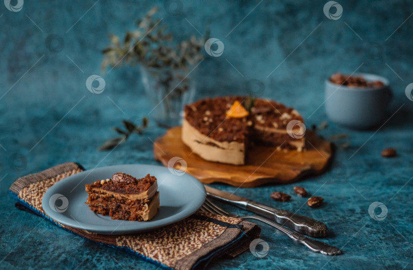 Скачать Домашний торт с шоколадом и кремом на круглой деревянной доске, тарелка с куском торта рядом с вилкой и ножом и кружка с орехами на темном фоне. Домашняя выпечка фотосток Ozero