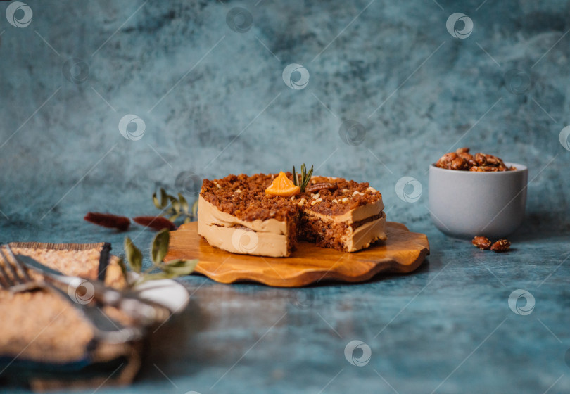 Скачать Домашний торт с шоколадом и кремом на круглой деревянной доске, тарелка с куском торта рядом с вилкой и ножом и кружка с орехами на темном фоне. фотосток Ozero