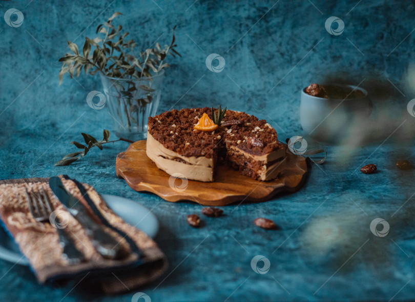 Скачать Домашний торт с шоколадом и кремом на круглой деревянной доске, тарелка с куском торта рядом с вилкой и ножом и кружка с орехами на темном фоне. Домашняя выпечка фотосток Ozero