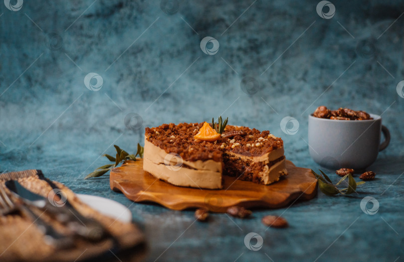 Скачать Домашний торт с шоколадом и кремом на круглой деревянной доске, тарелка с куском торта рядом с вилкой и ножом и кружка с орехами на темном фоне. фотосток Ozero