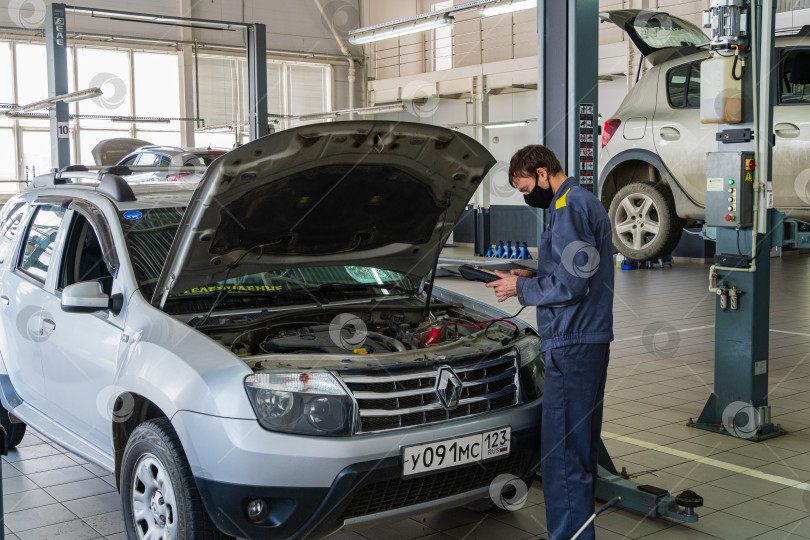 Скачать Автосалон Renault в Адыгее. Слесарь работает в защитной маске. Техническое обслуживание автомобиля Renault Duster. Карантин. Коронавирус (Covid-19). Пандемия. фотосток Ozero