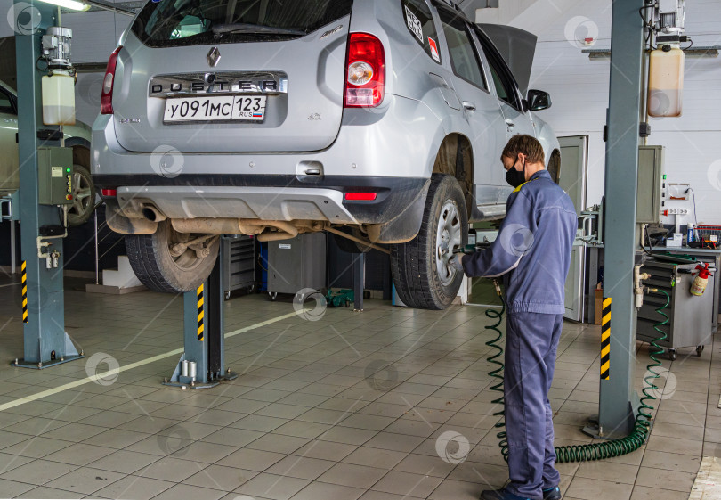 Скачать Автосалон Renault в Адыгее. Слесарь работает в защитной маске. Техническое обслуживание автомобиля Renault Duster. Карантин. Коронавирус (Covid-19). Пандемия. фотосток Ozero