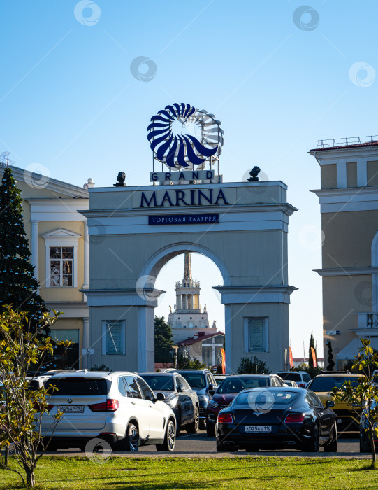 Скачать Торговая галерея Grand Marina в морском порту Сочи со стороны автостоянки. Здание морского порта Сочи в арке торговой галереи. Рождественская елка слева от арки. фотосток Ozero