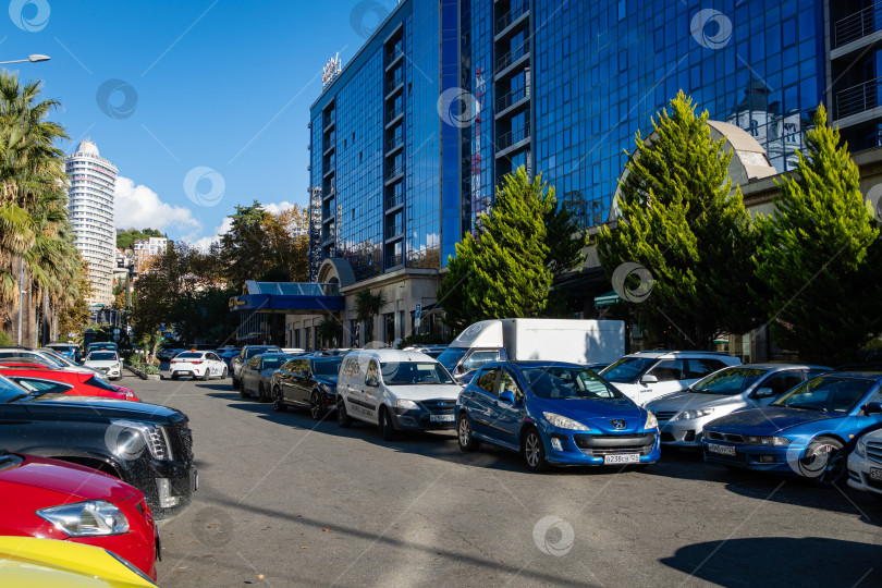 Скачать Припаркованные автомобили на одной из центральных улиц курортного города. Справа вдоль улицы находится большой гостиничный комплекс. Фасад здания покрыт голубым остеклением. фотосток Ozero