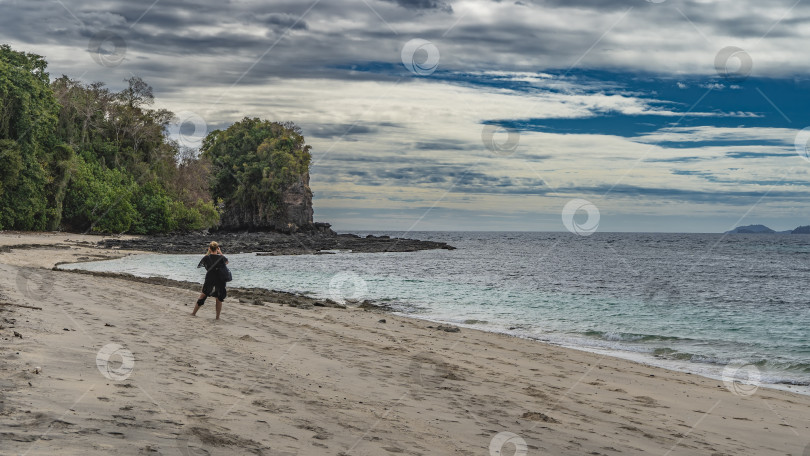 Скачать Девушка стоит на песчаном пляже, фотографируя живописную скалу. фотосток Ozero