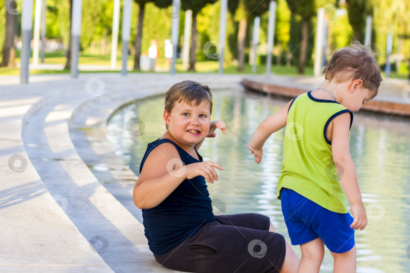 Скачать Дети в парке окунают ноги в фонтан, они очень счастливы. Веселитесь и радуйтесь летнему дню у фонтана. фотосток Ozero