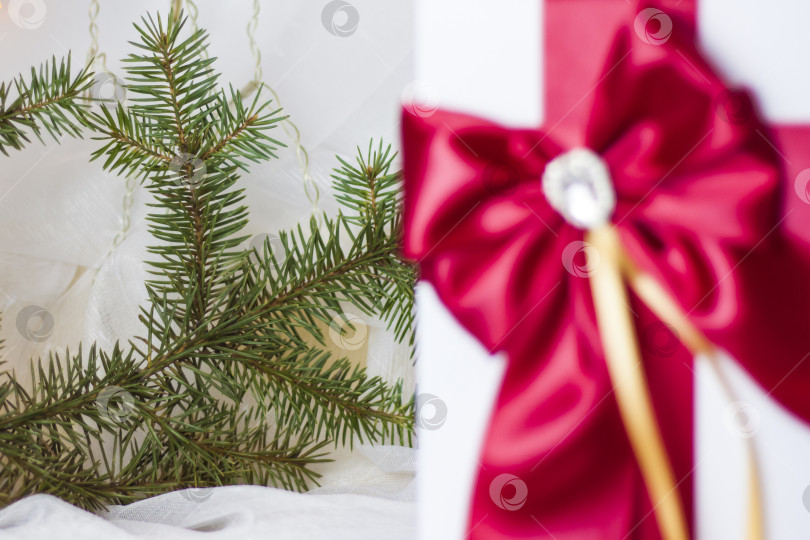 Скачать Рождественский подарок, украшенный красивым бантом на светлом фоне с еловой веточкой. Подарки, радость, сюрприз. Избирательный фокус. концепция Рождества и Нового года фотосток Ozero