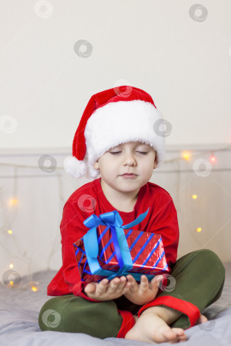 Скачать Портрет симпатичного мальчика в шапке Санта-Клауса. Забавный улыбающийся ребенок. Подарки, игрушки, радость, праздник. фотосток Ozero