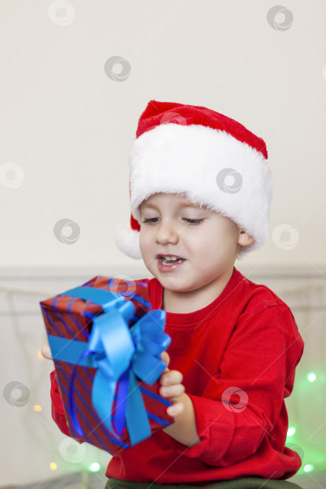 Скачать Портрет симпатичного мальчика в шапке Санта-Клауса. Забавный улыбающийся ребенок. Подарки, игрушки, радость, праздник. фотосток Ozero