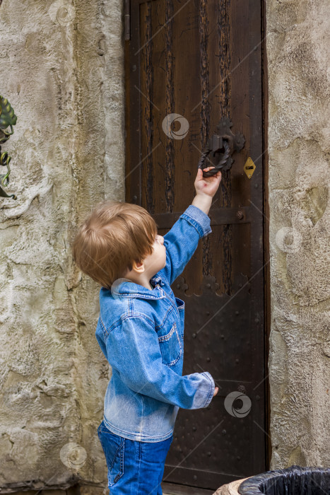 Скачать Маленький мальчик стоит и пытается открыть старую мощную дверь. фотосток Ozero