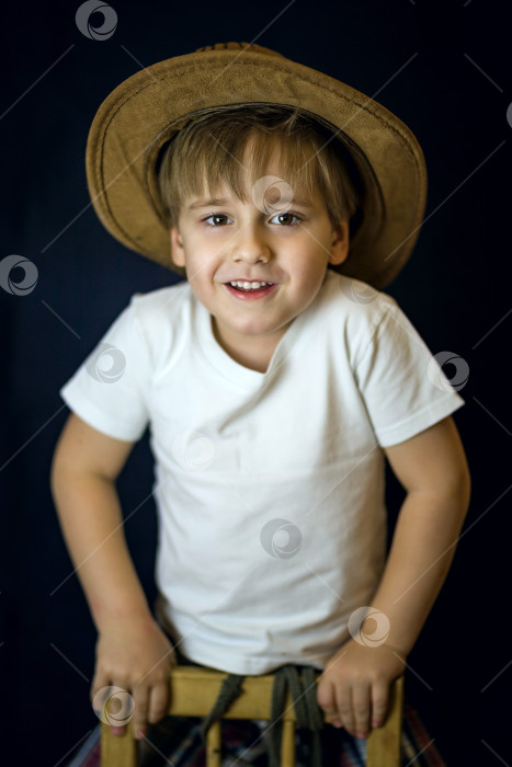 Скачать Лаконичный портрет европейского мальчика. Портрет на темном фоне мальчика в ковбойской шляпе и белой футболке. фотосток Ozero