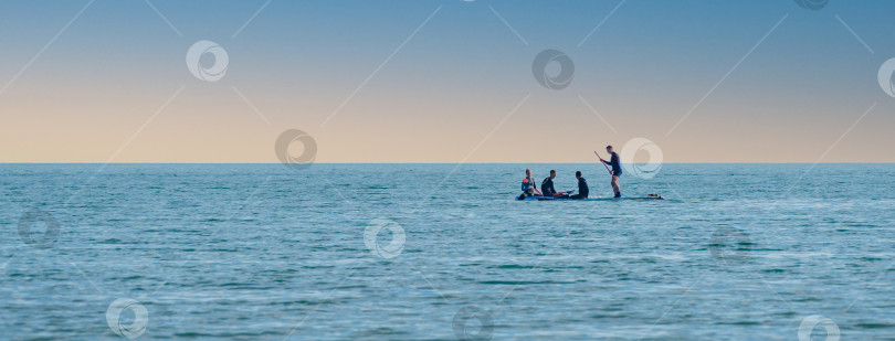 Скачать Молодые люди занимаются водными видами спорта в Черном море на фоне красивого неба. Мужчина с веслом стоит на надувной доске или SUP. Архипо-Осиповка Геленджик, Россия, 14 мая 2021 года фотосток Ozero