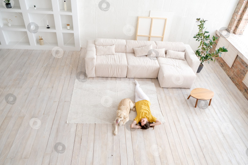 Скачать Портрет счастливой молодой женщины с домашней собакой, сидящей на полу дома. Белая женщина обнимает золотистого ретривера в гостиной фотосток Ozero