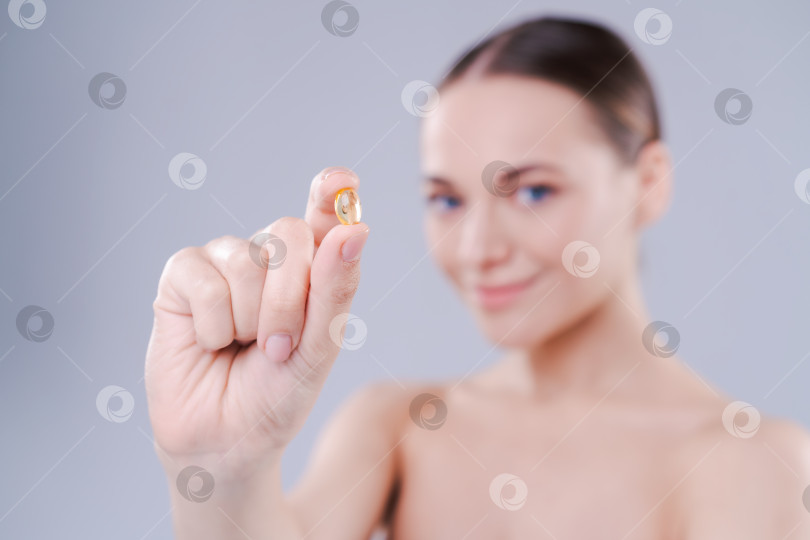 Скачать Привлекательная молодая женщина держит масляную таблетку omega capsule возле лица, концепция здоровья и молодости на светлом фоне студии. фотосток Ozero
