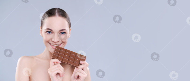 Скачать Крупным планом красивая девушка, радостно кусающая шоколадку на белом фоне, студийный снимок. фотосток Ozero