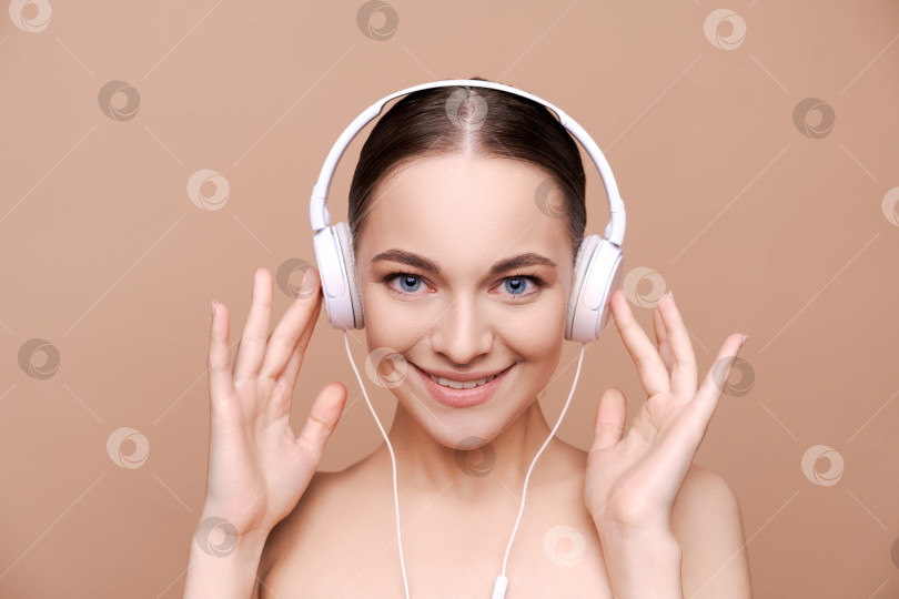Скачать улыбающаяся привлекательная женщина слушает музыку в наушниках на бежевом фоне. фотосток Ozero