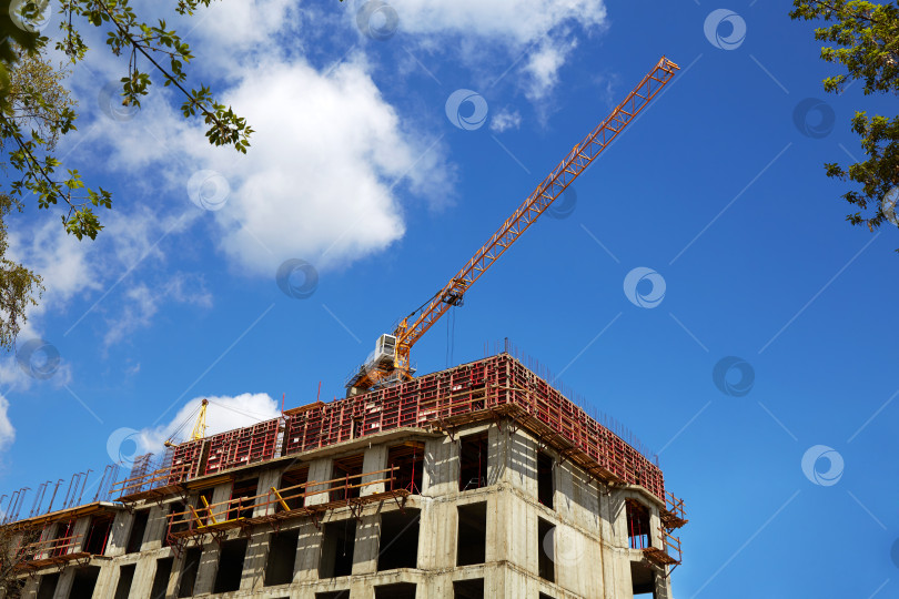Скачать Подъемный кран на строительной площадке. Строительство многоквартирного дома, голубое небо. фотосток Ozero