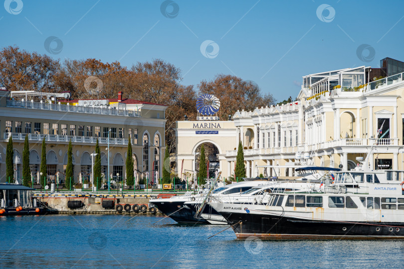 Скачать Катера и яхты пришвартованы к причалам Сочинского морского торгового порта. На заднем плане - торговая галерея Grand Marina. Зимний солнечный день. Чайки сидят на воде. фотосток Ozero