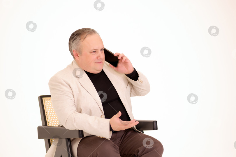 Скачать мужчина сидит в кресле и разговаривает по телефону на белом фоне фотосток Ozero
