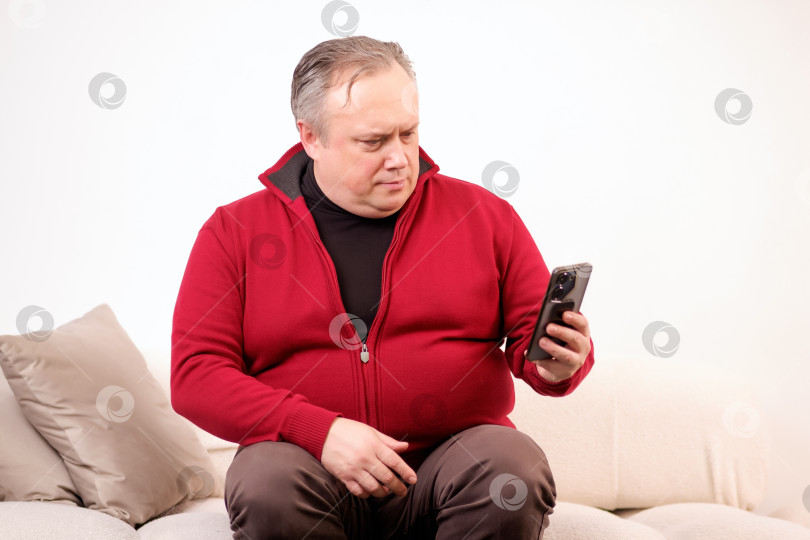 Скачать мужчина разговаривает или смотрит что-то по своему телефону, сидя на диване фотосток Ozero