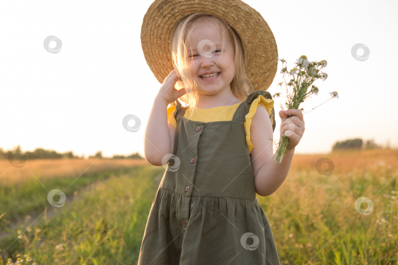 Скачать Маленькая светловолосая девочка в соломенной шляпке прогуливается по полю с букетом ромашек. Концепция прогулок на природе, свободы и экологически чистого образа жизни. фотосток Ozero