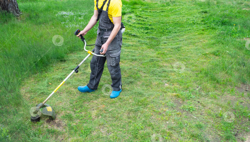 Скачать Мужчина-садовник подстригает зеленую траву на газоне на заднем дворе бензиновой косилкой. Триммер для ухода за садовым участком фотосток Ozero