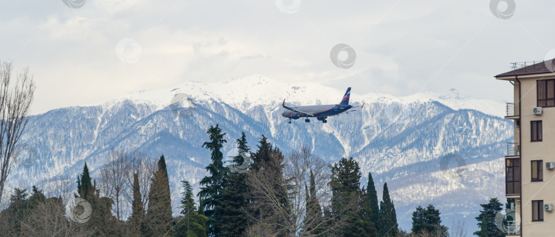 Скачать Самолет Airbus A321 авиакомпании "Аэрофлот Российские авиалинии" летит на фоне заснеженных вершин Кавказских гор и жилых зданий в поселке Сириус напротив Адлера. Сочи, Россия - 16 марта 2021 г. фотосток Ozero