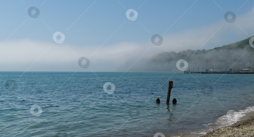 Скачать Красивый морской пейзаж. Туман опустился на пляж с голубой водой Черного моря. Большой якорь вертикально стоит на мелководье у берега.  Курорт Архипо-Осиповка фотосток Ozero