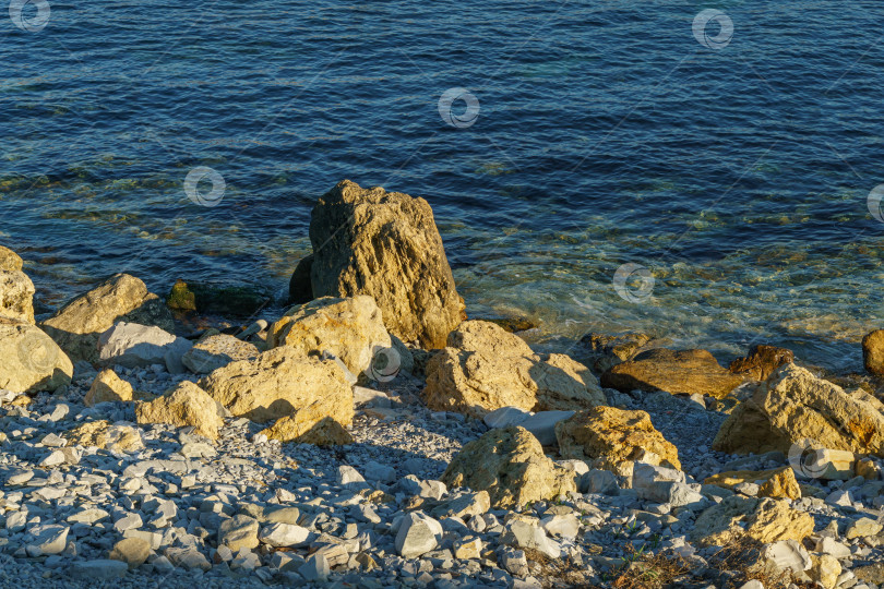 Скачать Большие желтые скалы на фоне синего моря на закате. Морские камни и утесы разных размеров и фактуры на пляже и под водой побережья Черного моря в качестве фона природы. фотосток Ozero