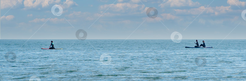 Скачать Молодые люди занимаются водными видами спорта в Черном море на фоне красивого неба.  Люди плавают на надувной доске или SUP.  Архипо-Осиповка, Геленджик, Россия, 14 мая 2021 года фотосток Ozero