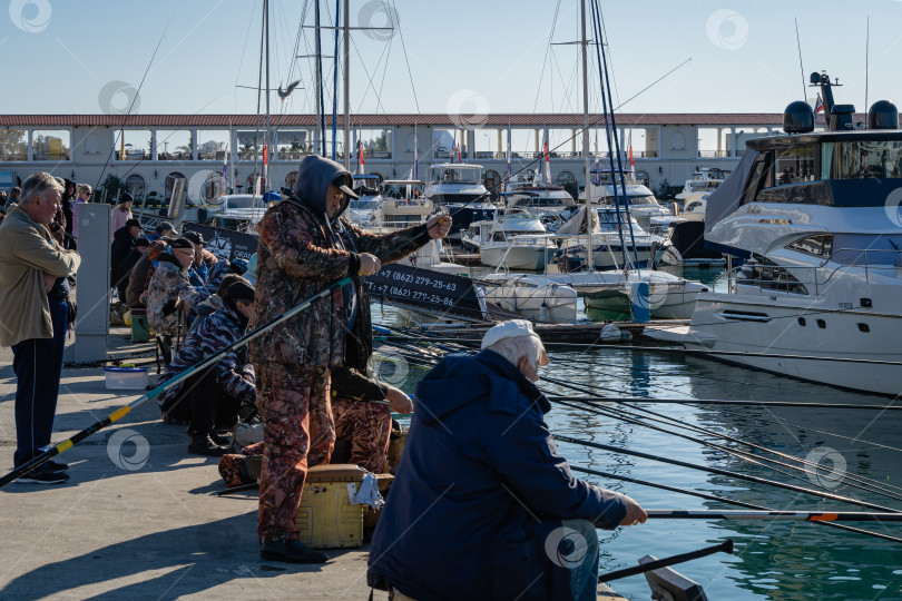 Скачать Рыбаки ловят рыбу у причалов Сочинского морского торгового порта. Крупный план. Рыбаки сидят с удочками на пирсе на фоне дорогих яхт. фотосток Ozero