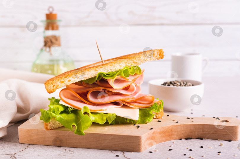 Скачать Бутерброд с ветчиной, сыром и луком на деревянной доске на столе фотосток Ozero