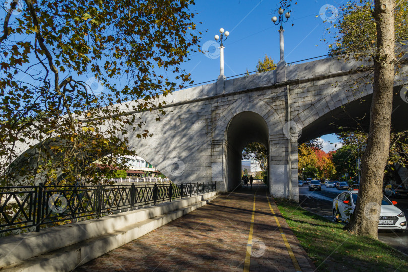 Скачать Каменная пешеходная арка под старым мостом Ривьера с проезжей частью в курортном городе Сочи. Любимый туристический маршрут для прогулок по набережной к Черному морю. Сочи, Россия - 25 ноября 2020 г. фотосток Ozero