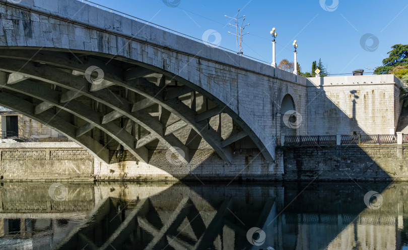 Скачать Вид на старый мост Ривьера через реку Сочи с отражением моста в воде. Осенний пейзаж в Сочи фотосток Ozero