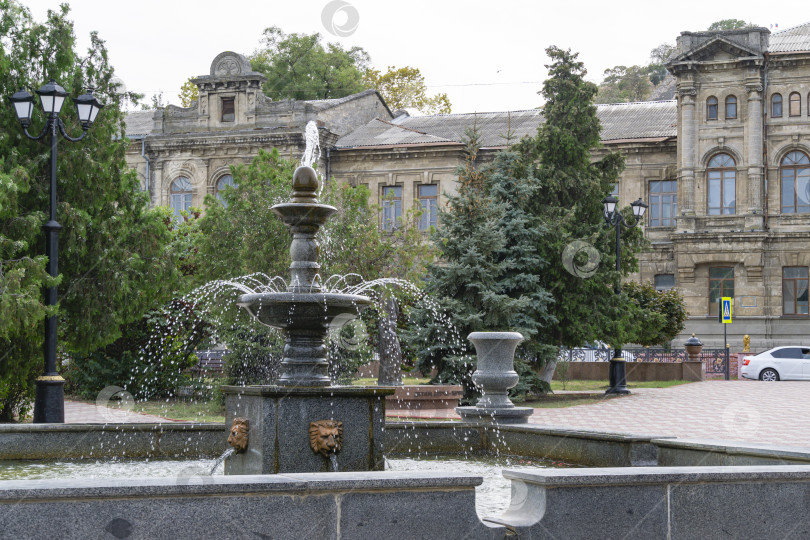 Скачать Городской фонтан в самом сердце исторического центра города Керчь на фоне серого здания бывшей женской гимназии. фотосток Ozero