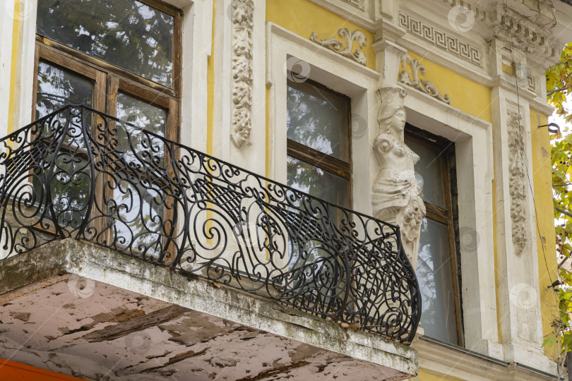 Скачать Элегантное оформление фасада старинного здания на улице Ленина в Керчи. Кованые элементы балкона и женская фигура на стене здания. фотосток Ozero