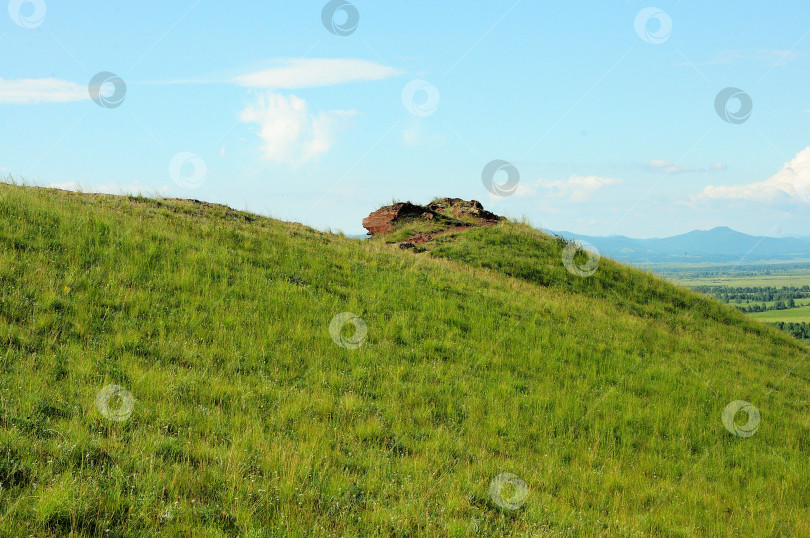 Скачать Остатки древней разрушенной стены из красного слоистого песчаника на вершине пологого холма с видом на живописную долину в солнечный летний день. фотосток Ozero
