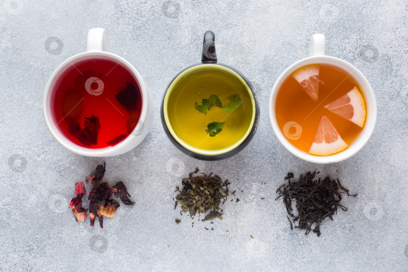 Скачать Чашки с разным чаем, красным, зеленым и черным, на сером столе фотосток Ozero