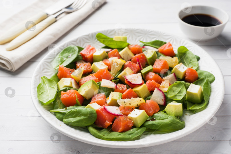 Скачать Выложите гавайский салат с лососем, авокадо, шпинатом и овощами в тарелку на белом столе. фотосток Ozero